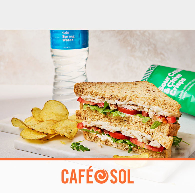 A hearty sandwich with chicken, tomatoes, and lettuce, served with crisps and a bottle of spring water, all branded Café Sol.