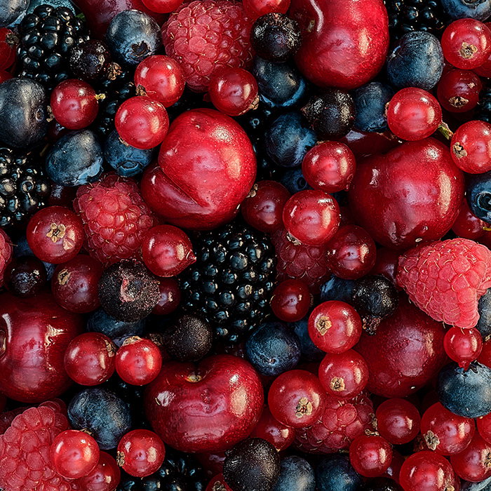 A vibrant collection of berries and fruits, including red currants, raspberries, blueberries, and blackberries, on a dark background.