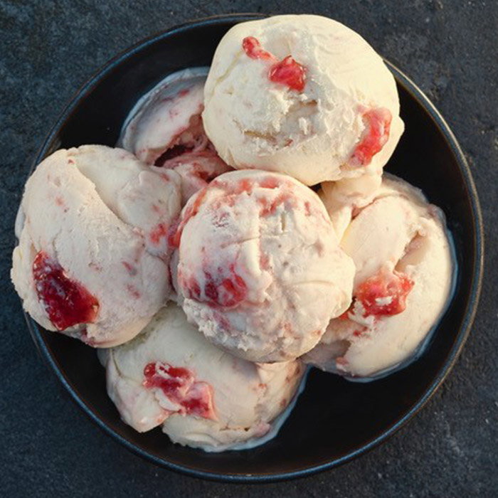 A bowl of creamy vanilla ice cream scoops swirled with vibrant red strawberry sauce.