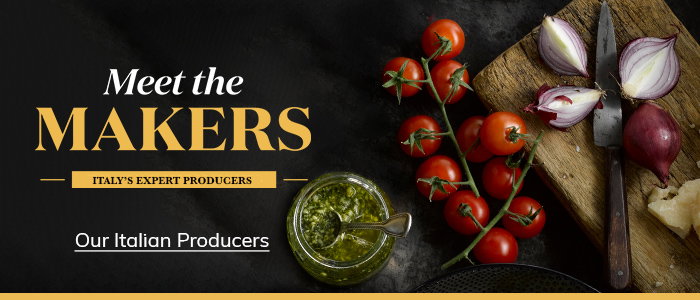 A wooden cutting board with tomatoes, red onions, and pesto, featuring the text "Meet the Makers: Italy's Expert Producers."