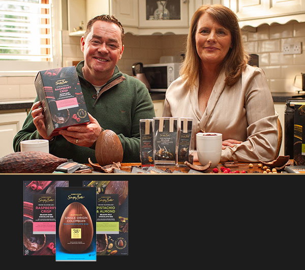  Ann Rudden and Neven Maguire display various chocolate bars and related products on a kitchen table, including a large chocolate egg and cocoa pod.
