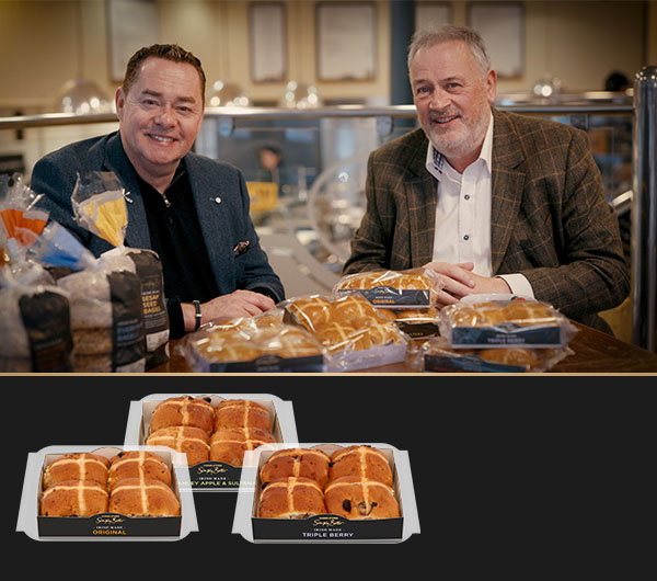 
Neven Maguire and Pat McCloskey sit at a table with packaged hot cross buns and various bread products in front of them.