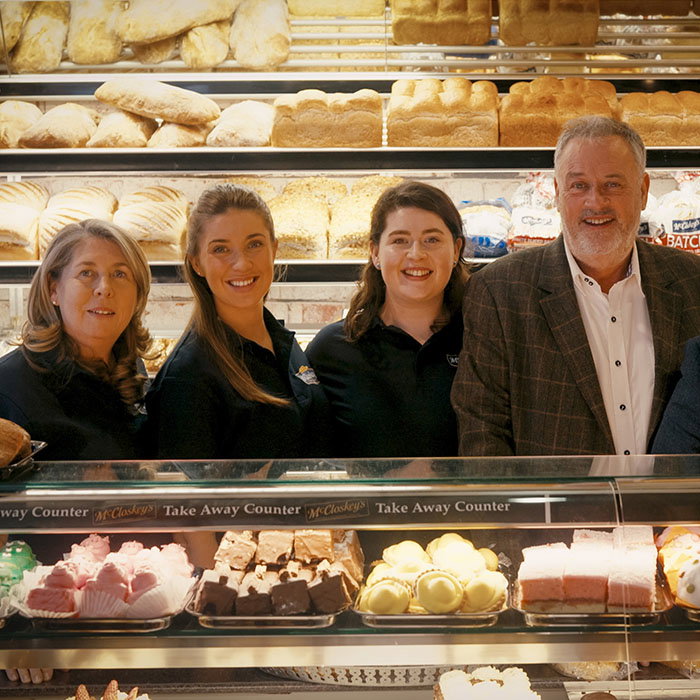 A bakery display featuring various pastries and breads, with staff members posing in front of a vibrant assortment of desserts.