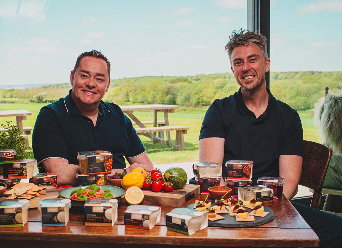 Neven Maguire and Chef Kevin Aherne with prepared dishes and food products at a dining table.