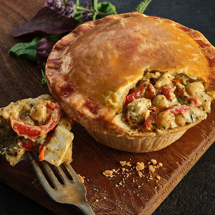 Golden-brown chicken pie with a flaky crust, revealing a savory filling of chicken, vegetables, and herbs, served on a wooden board.