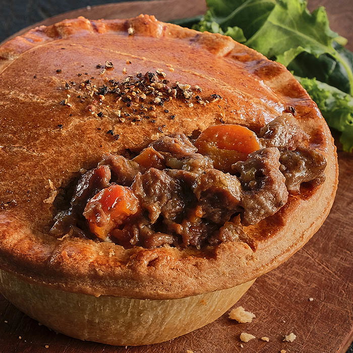 Golden-brown meat pie with a flaky crust, revealing savory filling of beef and carrots, accompanied by a side of fresh greens.