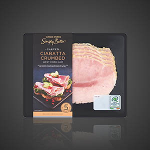 Pack of Dunnes Stores Simply Better carved ciabatta crumbed ham slices, with deli meat visible in a black tray, on a dark background