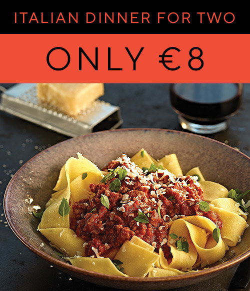 A plate of pappardelle pasta topped with rich meat sauce, garnished with herbs, accompanied by a glass of red wine. Promo: &euro;8 for two.
