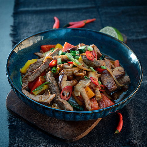 Bowl of beef stir-fry with sliced peppers, mushrooms, spring onions and red chilli in a savoury sauce.