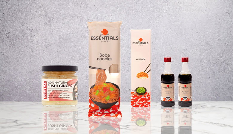 An assortment of Asian ingredients: sushi ginger, soba noodles, wasabi, and sweet soy sauce on a marble countertop with a gray background.