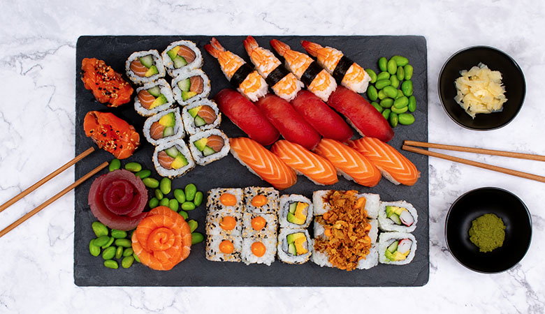 A beautifully arranged sushi platter featuring various rolls, sashimi, and edamame, accompanied by ginger, wasabi, and chopsticks.