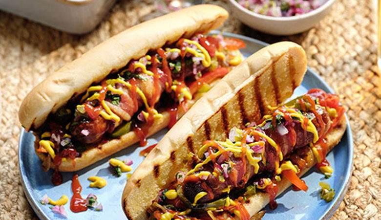 Two grilled hot dog buns overflowing with colorful toppings, including mustard, ketchup, and diced vegetables, on a blue plate.