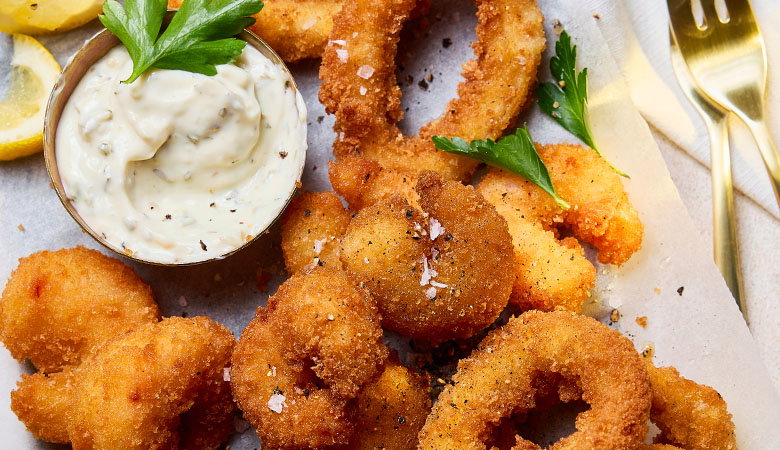 Golden-brown beer-battered cod fish fingers with flaky white fish visible inside, served with lemon wedges and garnished with fresh parsley on a white plate