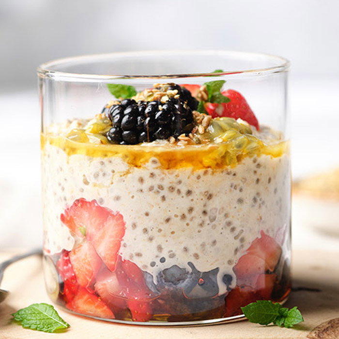 Chia seed pudding in a glass jar layered with fresh strawberries, blueberries, blackberries, passion fruit, and garnished with mint leaves.