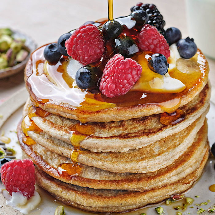 Stack of fluffy pancakes topped with fresh berries, drizzled with syrup, and a dollop of cream on a rustic plate. beautifully baked meat pie with a golden crust, revealing layers of turkey, ham, and stuffing on a wooden board.