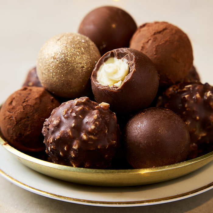 A plate of assorted chocolate truffles, including a gold glittered one and a bitten truffle revealing a creamy filling. The image evokes indulgence.