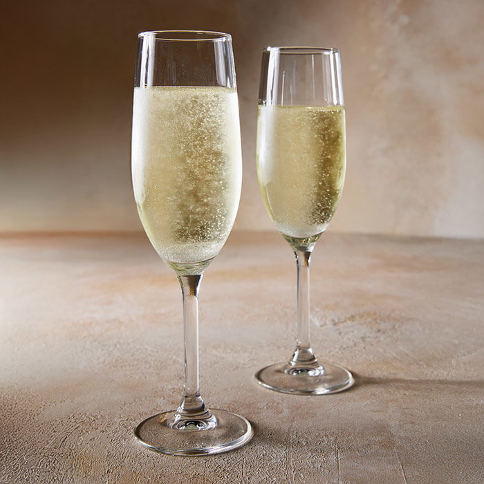 Two champagne flutes filled with bubbly, golden liquid sit on a textured surface. The scene is elegant and celebratory, with soft lighting.