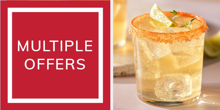 a tumbler glasses with yellow liquid and a sliced lime inside, ice cubes and an orange salted rim