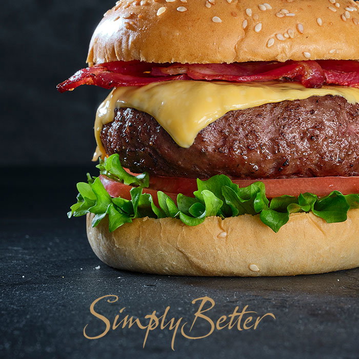 Close-up of a cheeseburger with bacon, lettuce, tomato, and a sesame seed bun on a dark surface with 