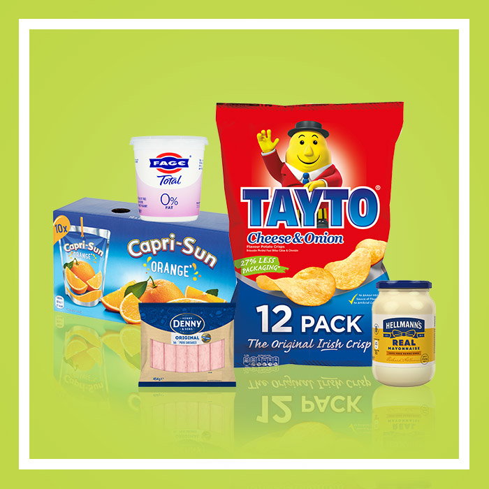 Selection of grocery items including Tayto Cheese & Onion crisps, Capri-Sun Orange drinks, low-fat yoghurt, sliced ham and mayonnaise on a green background.