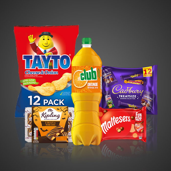 Halloween promotional food and snack bundle featuring Tayto Cheese & Onion crisps, Club Orange drink, Cadbury treats, Maltesers Fun Size chocolates and Mr Kipling chocolate orange slices on a dark background.