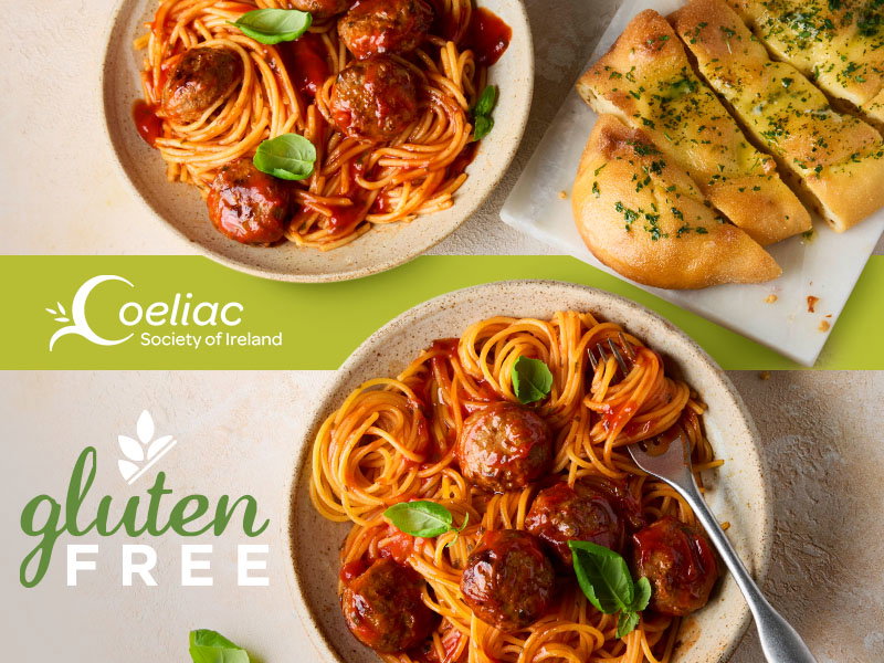 Two bowls of gluten-free spaghetti and meatballs garnished with basil, served alongside gluten-free garlic bread slices.