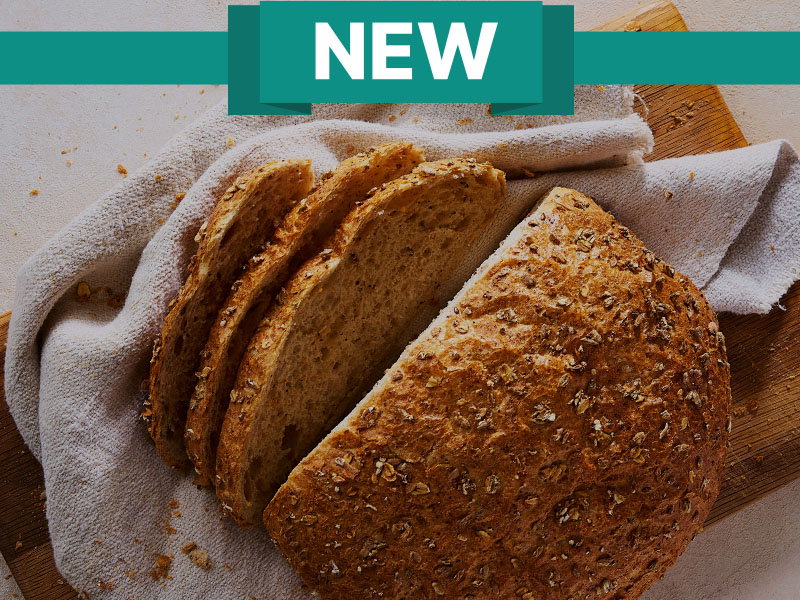 New multigrain bread loaf partially sliced on a wooden cutting board with a cloth underneath.