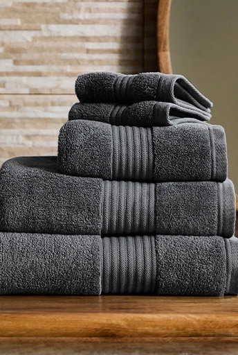Stack of dark grey folded bath towels on a wooden surface.