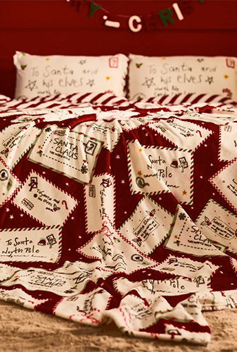 Christmas-themed bedding with festive letter-pattern print, including pillows addressed to Santa and his elves.