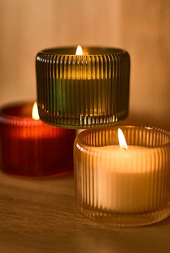 Three lit Dunnes Stores candles in ribbed glass holders on a wooden surface, creating a warm ambient glow.
