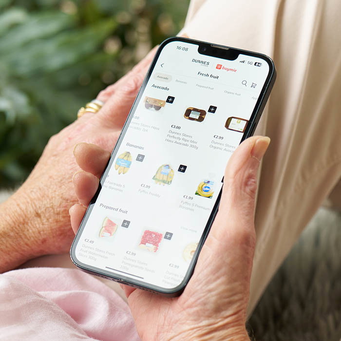Person holding a smartphone displaying the Dunnes Stores app, featuring various grocery products.