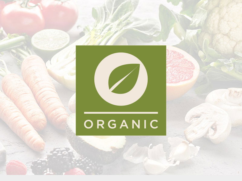 Fresh organic vegetables including carrots, potatoes, and leafy greens with green 'ORGANIC' label featuring leaf icon in cream circle.