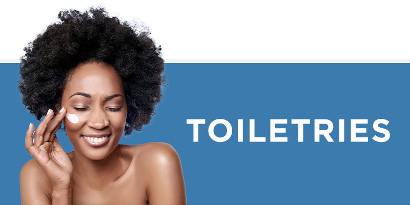 Beauty and skincare advertisement featuring a smiling woman with natural curly hair applying white cream or moisturiser to her face. Large white text reads 'TOILETRIES' against a soft blue background.