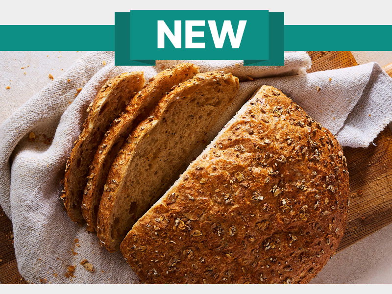 New multigrain bread loaf partially sliced on a wooden cutting board with a cloth underneath.