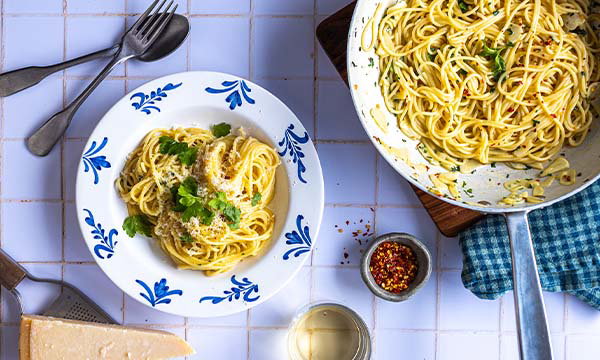 Plate of aglio olio spaghetti garnished with parsley, served beside