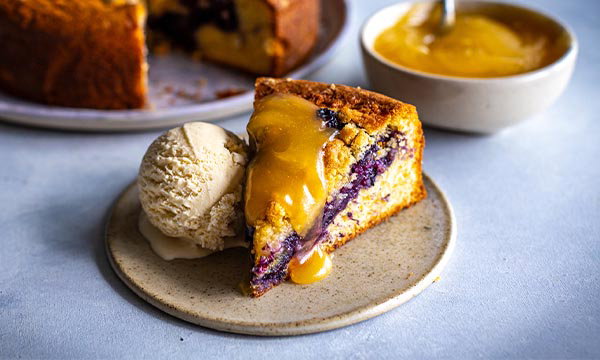 Slice of blueberry crumble cake served with vanilla ice cream and warm custard.