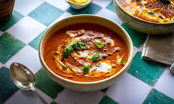 Bowl of roasted tomato and garlic soup topped with cream, herbs and crispy croutons.