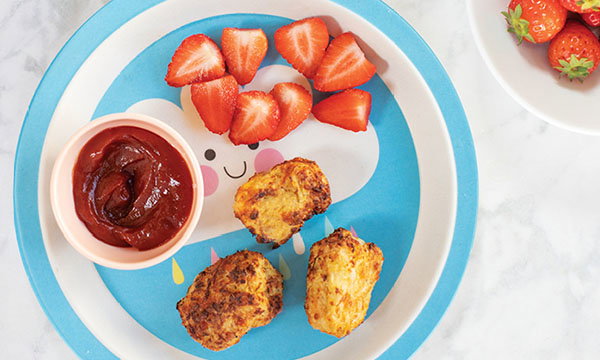 A colourful plate with cloud design holds crispy nuggets, sliced strawberries, and a cup of sauce, conveying a cheerful and playful dining experience.