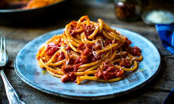 A plate of spaghetti with rich red tomato sauce, garnished with grated cheese, sits on a rustic wooden table, creating a warm and hearty dining atmosphere.