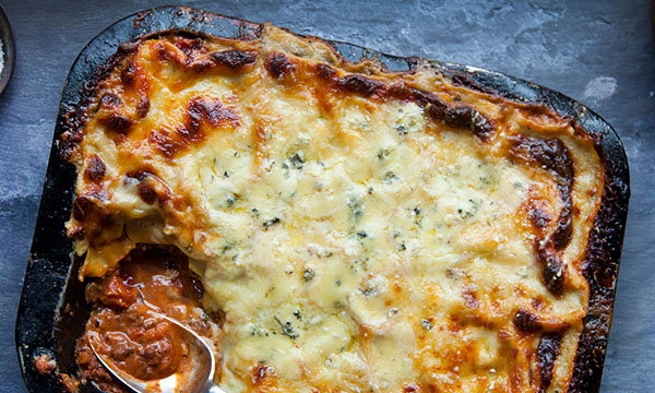 Golden, bubbly lasagna with a serving missing, revealing rich, meaty layers beneath. Edges are crispy and browned, creating a warm, inviting feel.