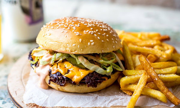 A juicy cheeseburger with lettuce, pickles, and sauce on a sesame seed bun next to crispy golden fries on parchment paper, evoking a classic takeaway feel.