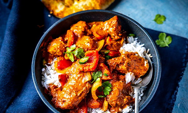 Chicken tikka masala served over white rice, with peppers and coriander garnish, in a rich spiced sauce
