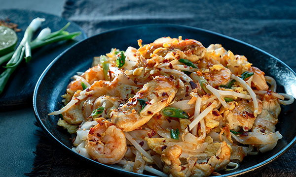 Prawn Pad Thai with rice noodles, bean sprouts, spring onions and scrambled egg, garnished with chilli flakes