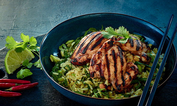 Grilled chicken on coriander-lime rice with garnish in a dark blue bowl; fresh lime, chili peppers, and coriander on the side. Cozy, appetising vibe.