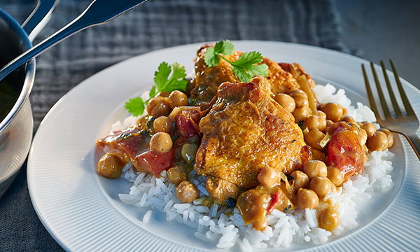 A plate of white rice topped with curry chicken, chickpeas, and red bell peppers, garnished with cilantro. The mood is appetizing and warm.