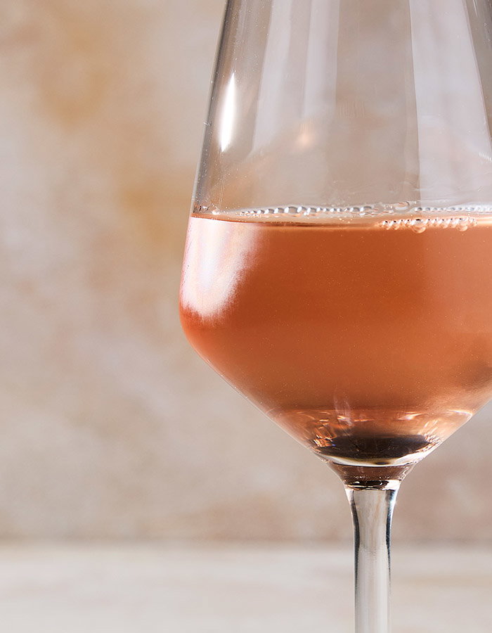 A glass of ros&eacute; wine with a soft peach hue, set against a blurred background, creating an elegant ambiance.