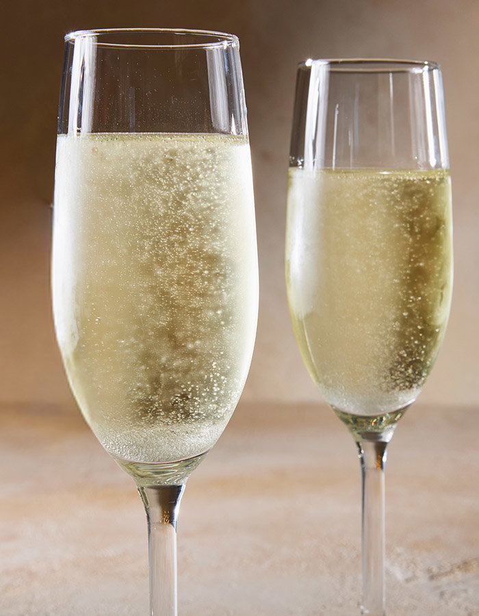 Two champagne flutes filled with bubbling champagne against a warm, softly blurred background