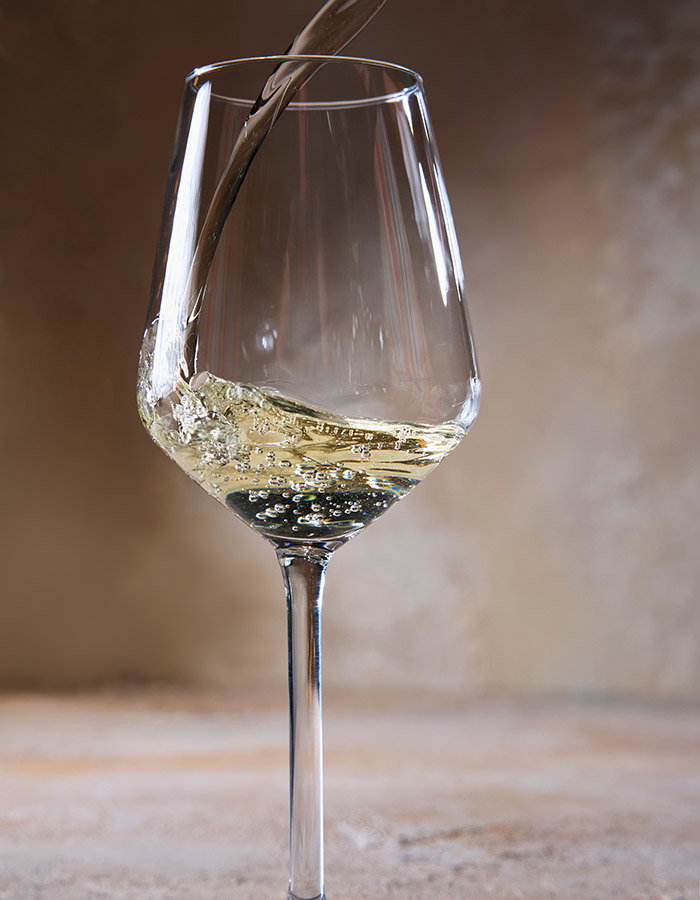 A glass of white wine being poured, set against a warm, softly blurred background
